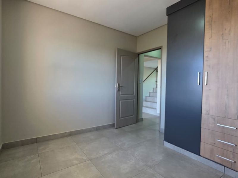 A bright, empty bedroom featuring modern tiled flooring, neutral walls, and contemporary built-in cupboards with a two-tone finish.