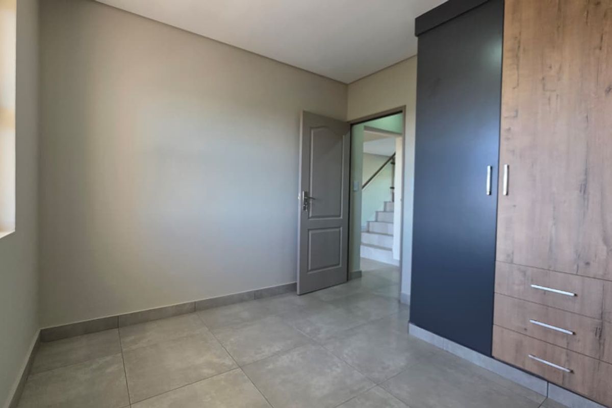 A bright, empty bedroom featuring modern tiled flooring, neutral walls, and contemporary built-in cupboards with a two-tone finish.