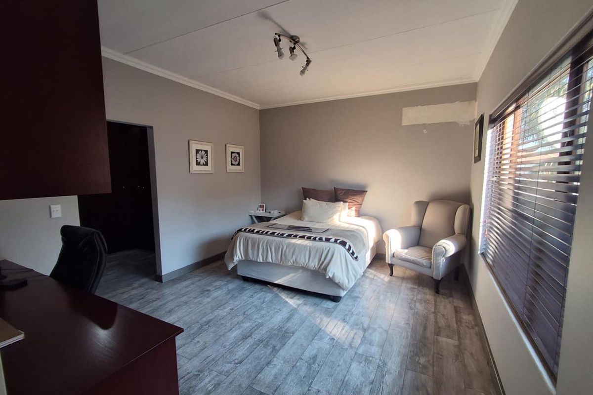 A bedroom featuring wood-look laminate flooring, neutral wall tones, and horizontal window blinds.