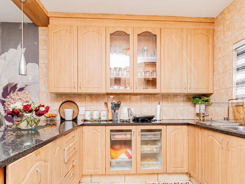 A functional kitchen featuring light wood-finish cabinetry, granite countertops, tiled backsplash, and a double basin sink with integrated storage solutions.