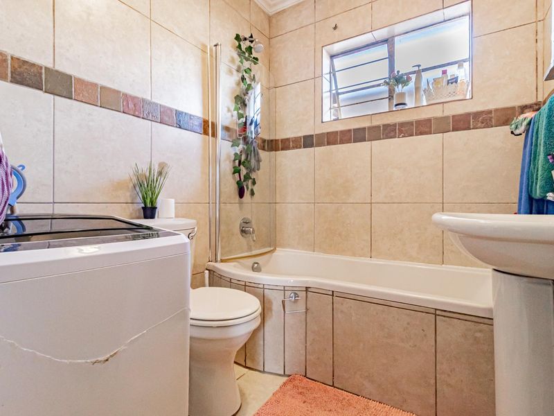 A functional bathroom featuring a bathtub with a glass screen, pedestal basin, and toilet, finished with neutral wall tiling.