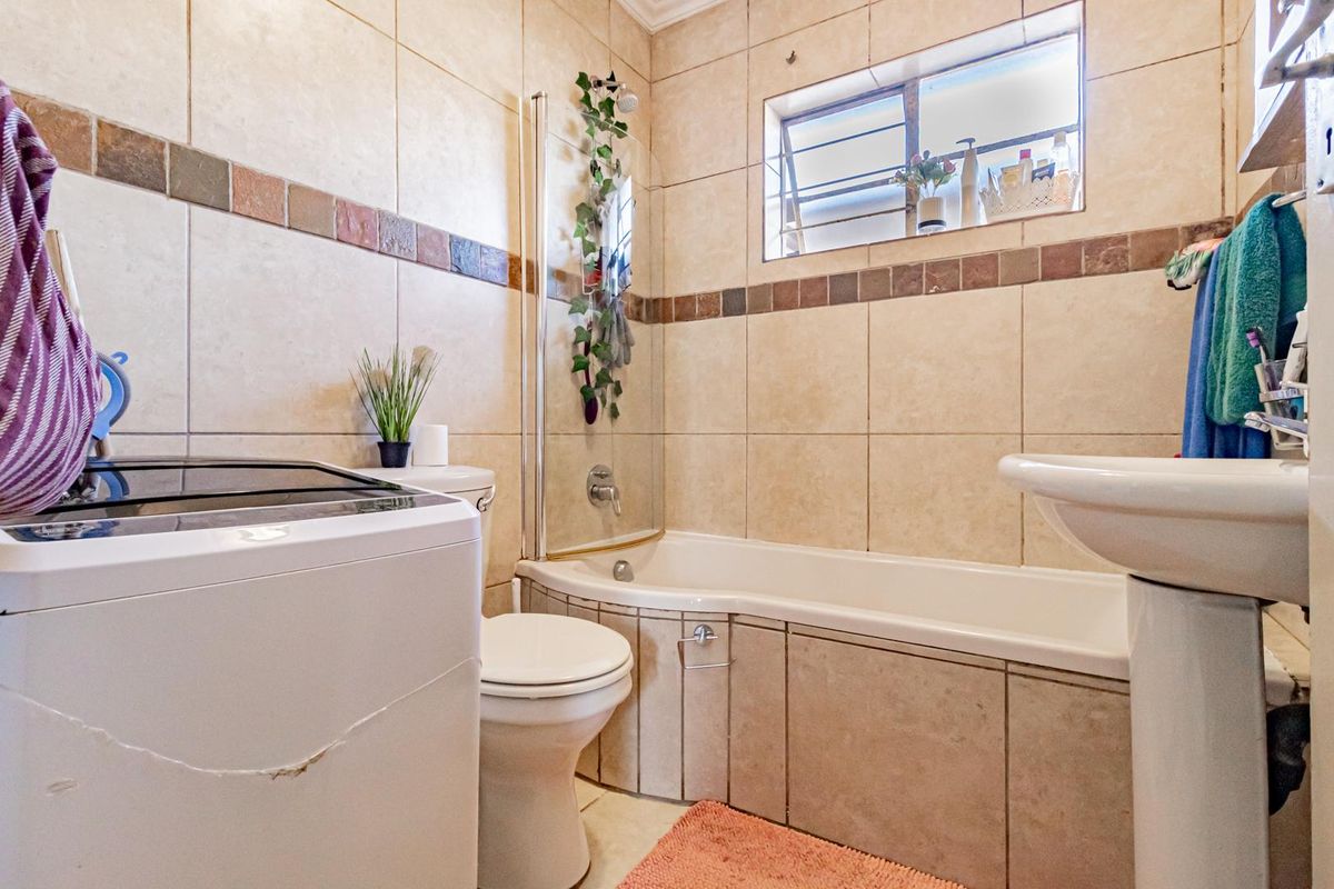A functional bathroom featuring a bathtub with a glass screen, pedestal basin, and toilet, finished with neutral wall tiling.