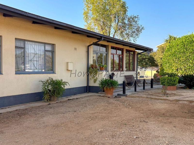 Rear exterior view of the house featuring plastered walls, metal window frames with security bars, and a gravel yard area.