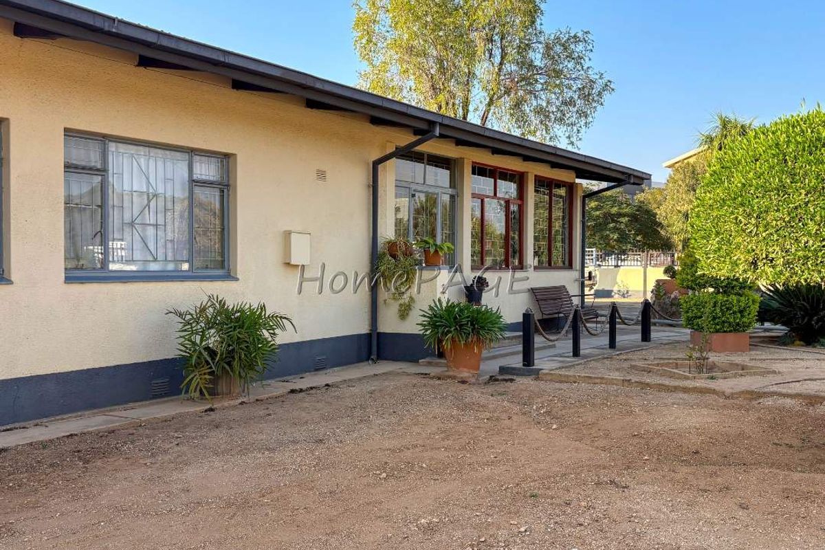 Rear exterior view of the house featuring plastered walls, metal window frames with security bars, and a gravel yard area.