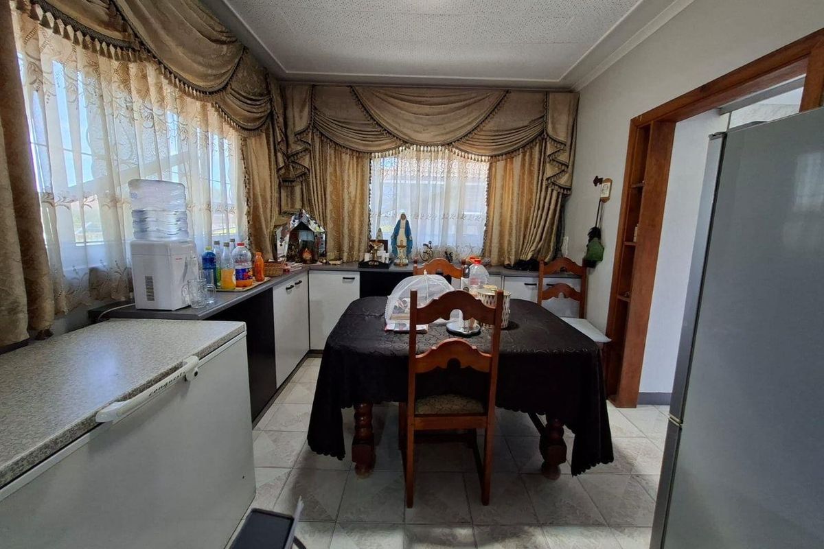 A functional kitchen and dining area featuring tiled flooring, built-in cabinetry, and large windows with decorative curtains.