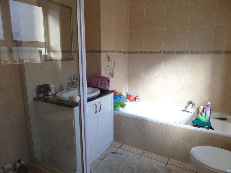 A functional bathroom featuring a built-in vanity with sink, a bathtub, a separate shower enclosure, and neutral wall and floor tiling.