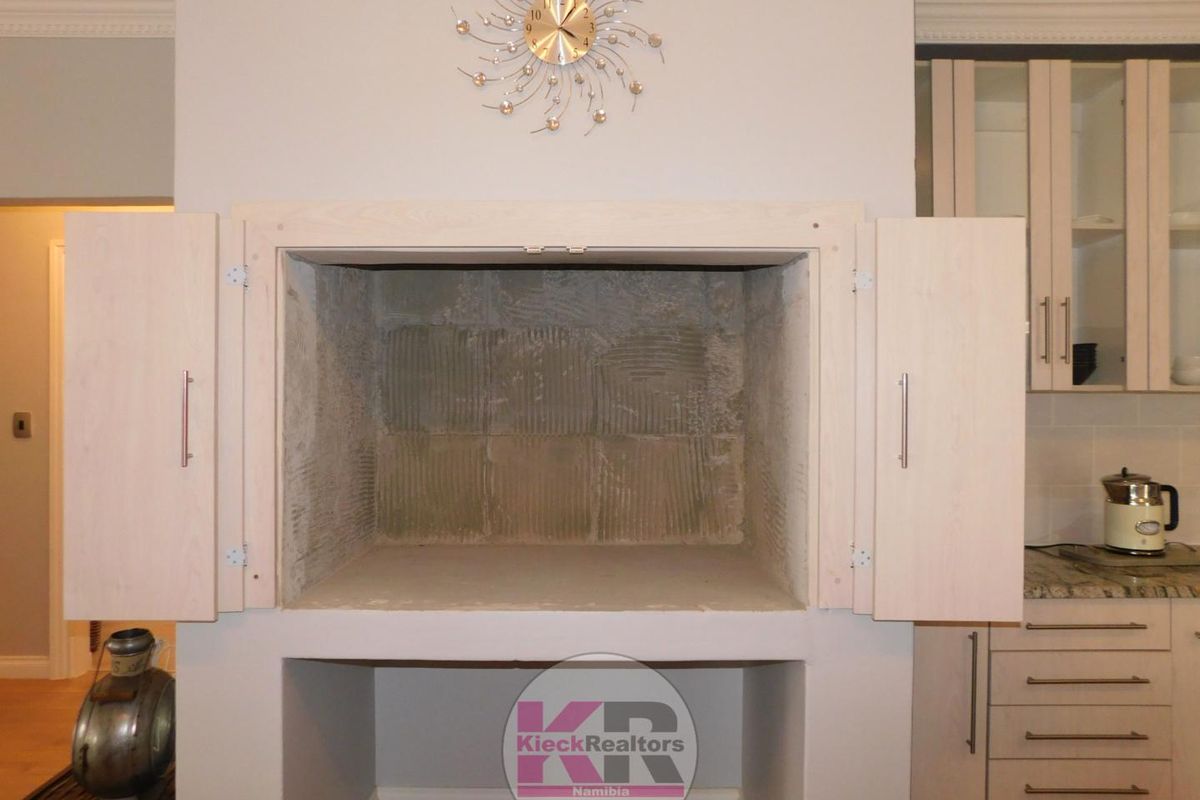A built-in fireplace feature with light wood cabinetry doors, currently showing unfinished interior masonry and exposed adhesive.