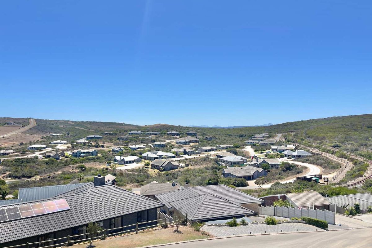 Elevated aerial view overlooking a residential estate with tiled roof houses, paved roads, and surrounding natural landscape.