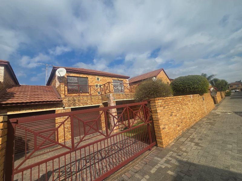 Front exterior view of a double-story townhouse featuring a brick facade, tiled roof, double garage, and a secure gated entrance.