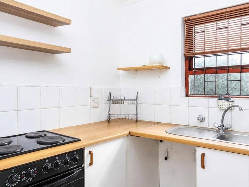 A functional kitchen featuring wooden countertops, built-in oven with electric hob, double sink, and floating shelving, offering a clean and practical workspace.