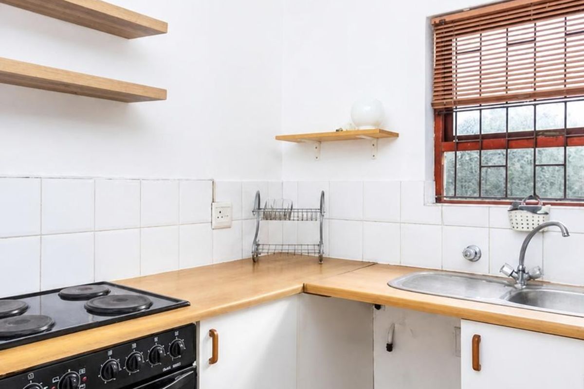 A functional kitchen featuring wooden countertops, built-in oven with electric hob, double sink, and floating shelving, offering a clean and practical workspace.