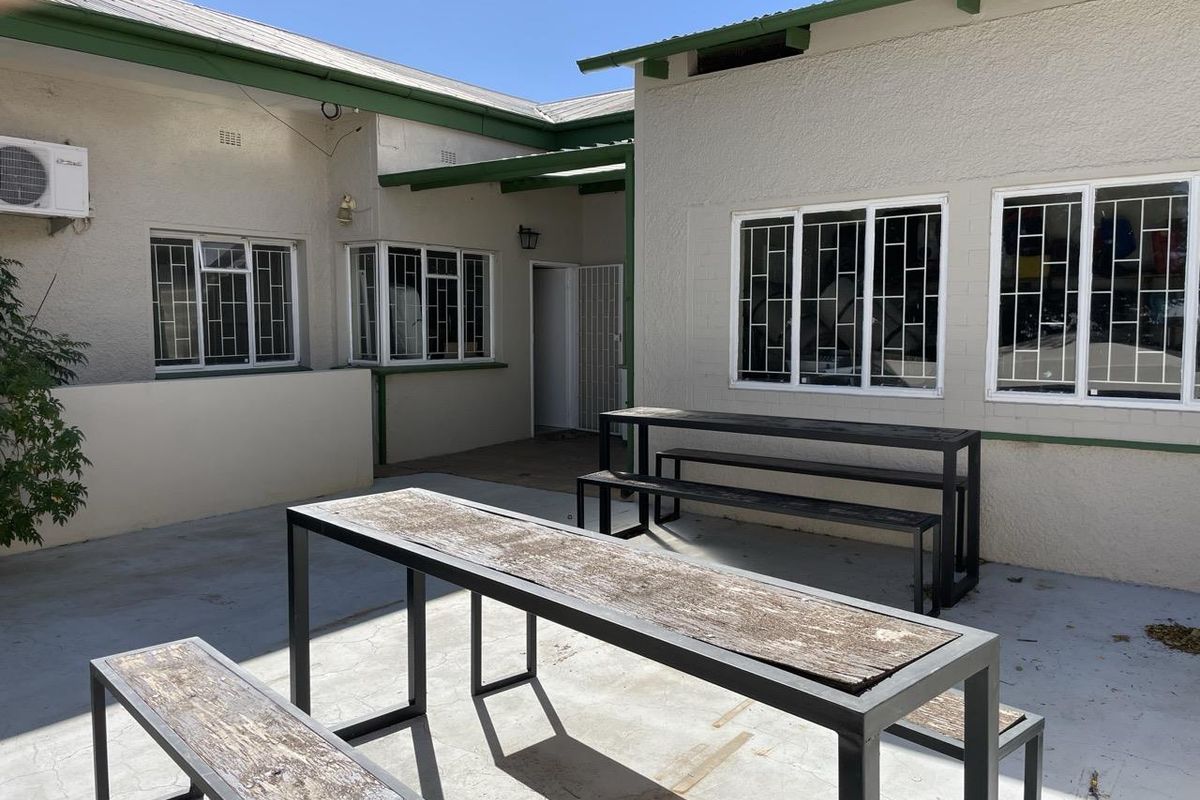 A paved outdoor courtyard area featuring a covered walkway, security bars on windows, and an external air conditioning unit.