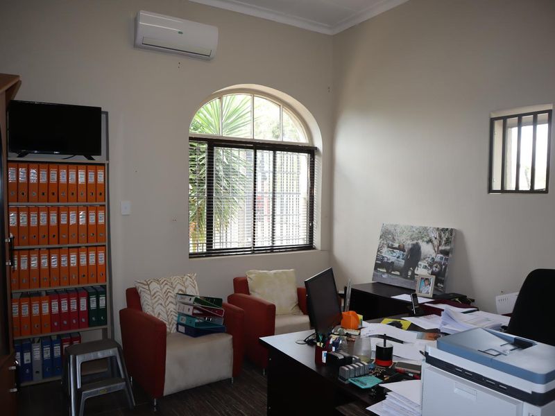 A functional office space featuring an arched window with security bars and a wall-mounted air conditioning unit.