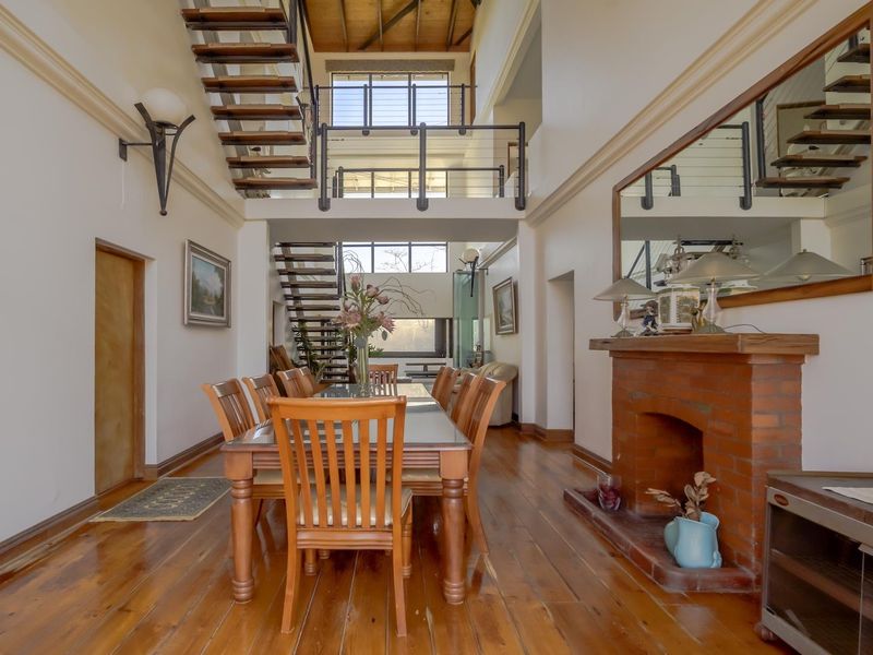 Spacious dining area featuring high vaulted timber ceilings, a brick fireplace, and an impressive open-tread staircase leading to a mezzanine level.