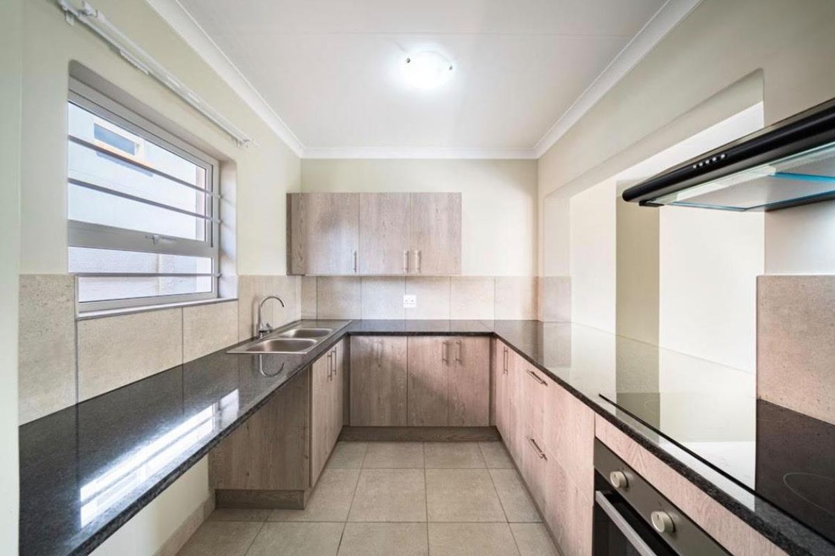 A functional kitchen featuring light wood-finish cabinetry, dark granite countertops, a double sink, and a built-in oven with an extractor fan.