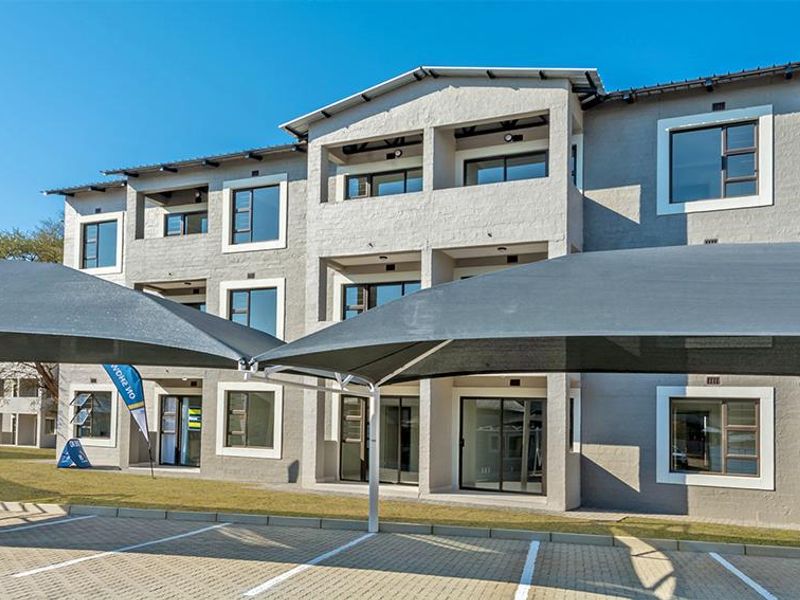 Front elevation of a modern apartment complex featuring paved parking with shade sails, balconies, and large aluminium-framed windows.