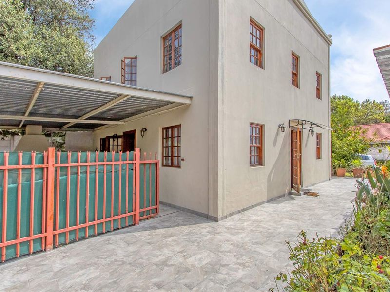 Rear exterior view of the property featuring a paved patio area, a covered carport, and established garden borders.