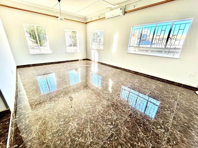 A bright, empty living room featuring polished marble-look floor tiles, split-system air conditioning, and large windows with security bars.