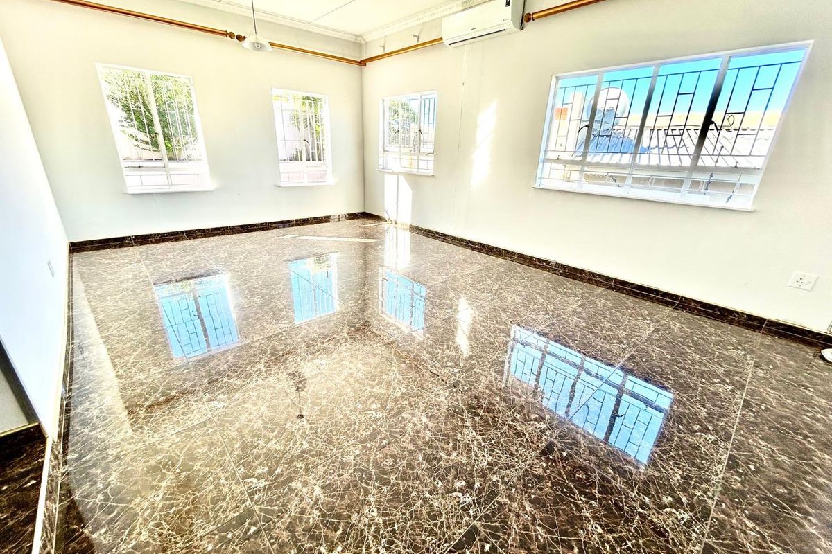 A bright, empty living room featuring polished marble-look floor tiles, split-system air conditioning, and large windows with security bars.
