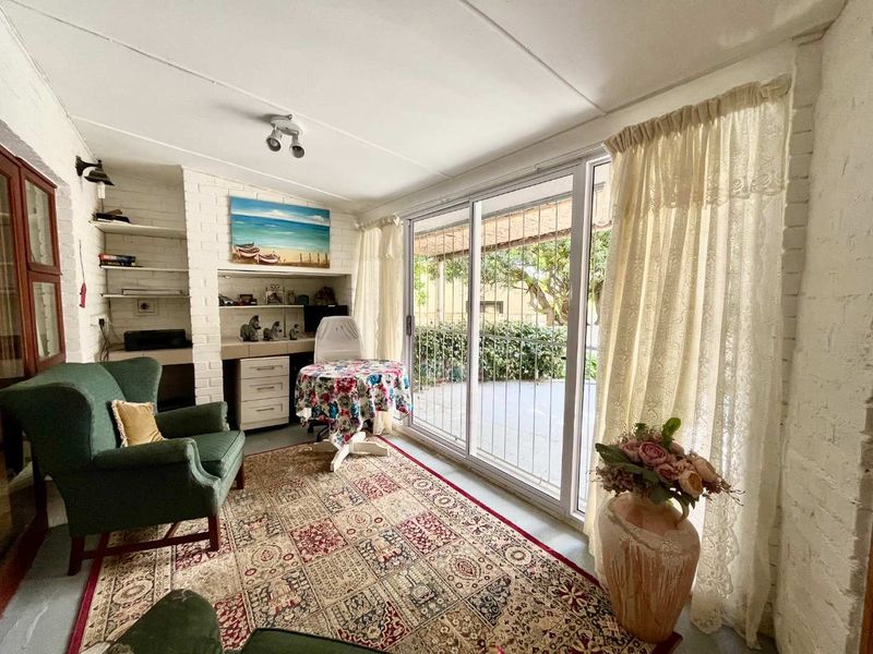 A sunlit living area featuring painted brick walls, built-in shelving, and large sliding glass doors that provide direct access to the outdoor patio.