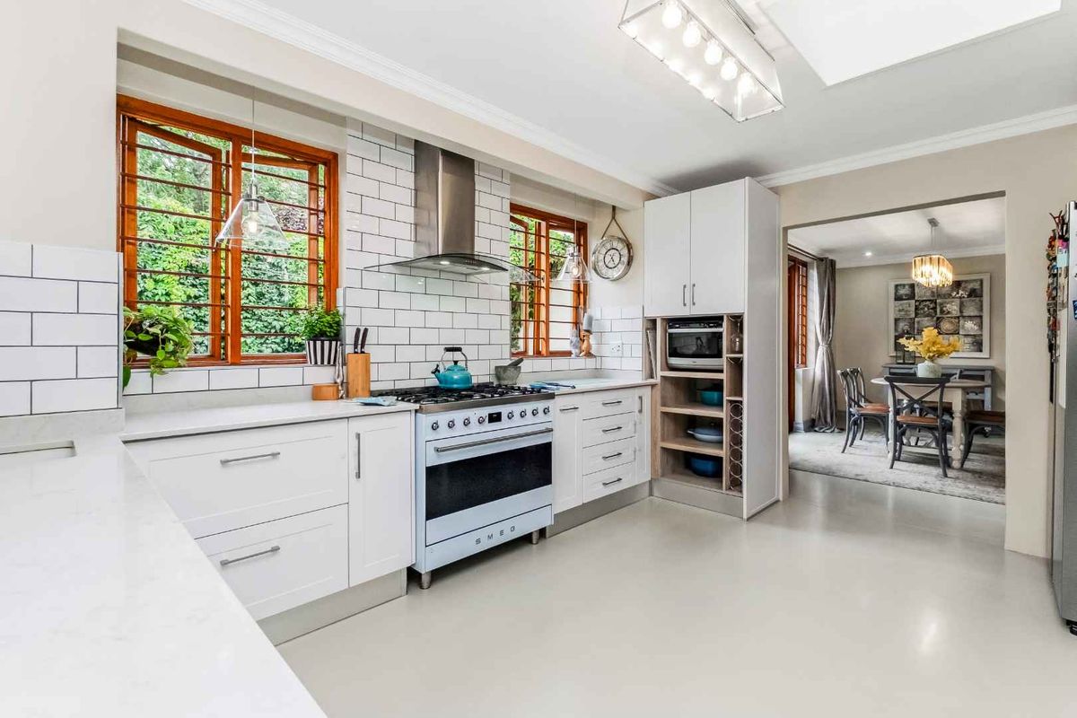 Modern kitchen featuring white cabinetry, subway tile backsplash, stainless steel extractor fan, and a freestanding Smeg oven, with an open-plan flow to the dining area.