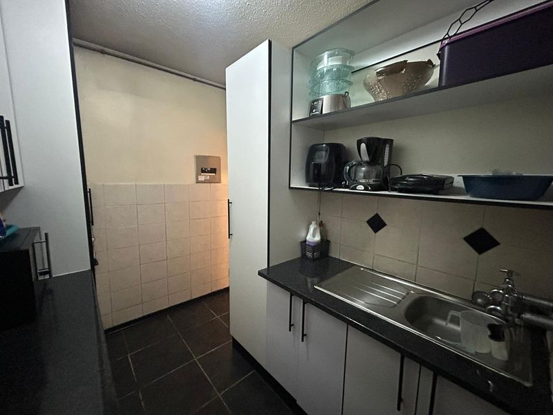 A compact kitchen featuring dark countertops, white cabinetry, a stainless steel sink, and open shelving, providing a functional prep and wash-up area.