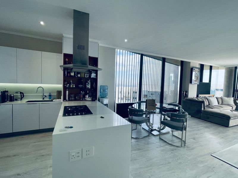 Modern open-plan apartment featuring a sleek kitchen with a central island, gas hob, and expansive floor-to-ceiling windows offering natural light and views.