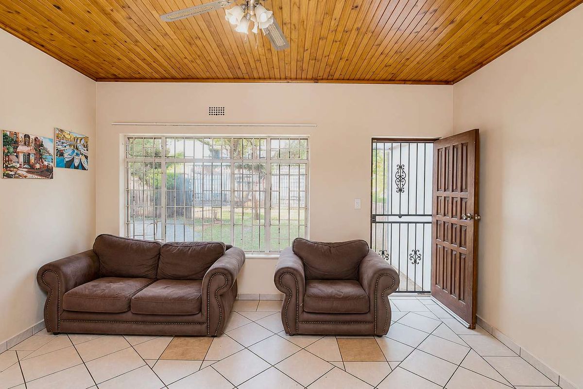 A living room featuring tiled flooring, a timber-paneled ceiling, a large window with security bars, and a wooden door with a security gate.