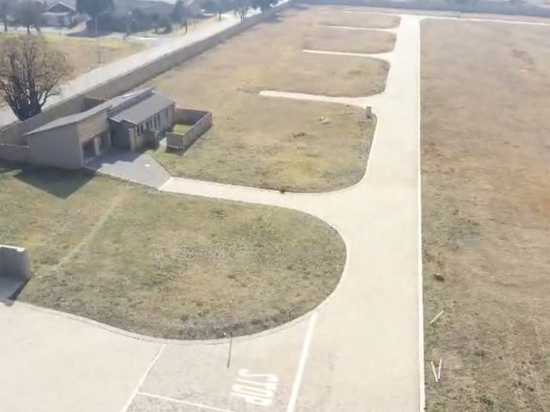Aerial view of a residential development site featuring paved access roads, boundary walls, and vacant land plots ready for construction.