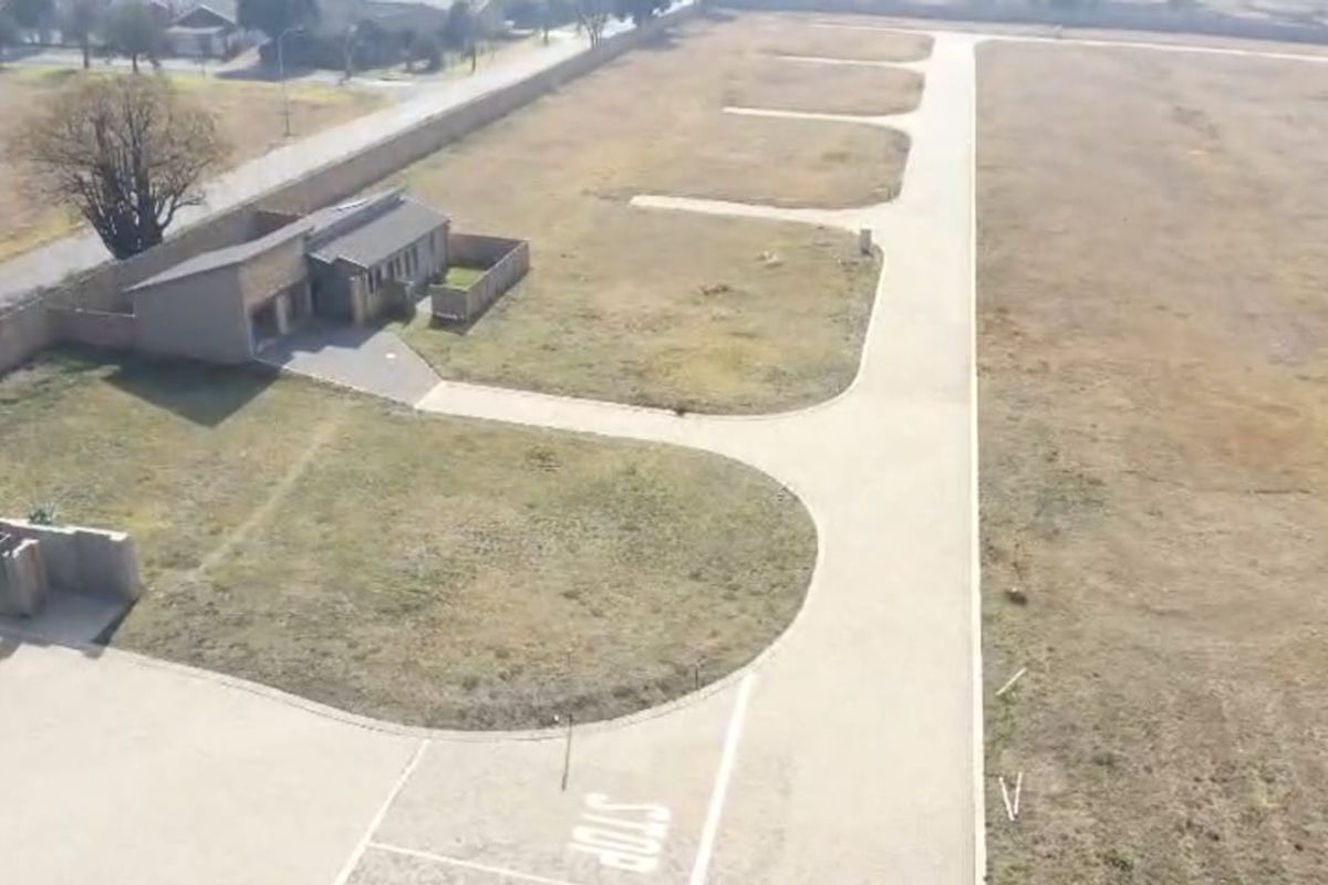 Aerial view of a residential development site featuring paved access roads, boundary walls, and vacant land plots ready for construction.
