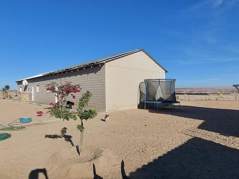 Rear view of a small holding property featuring concrete block construction, solar panels, and an expansive sandy yard area.