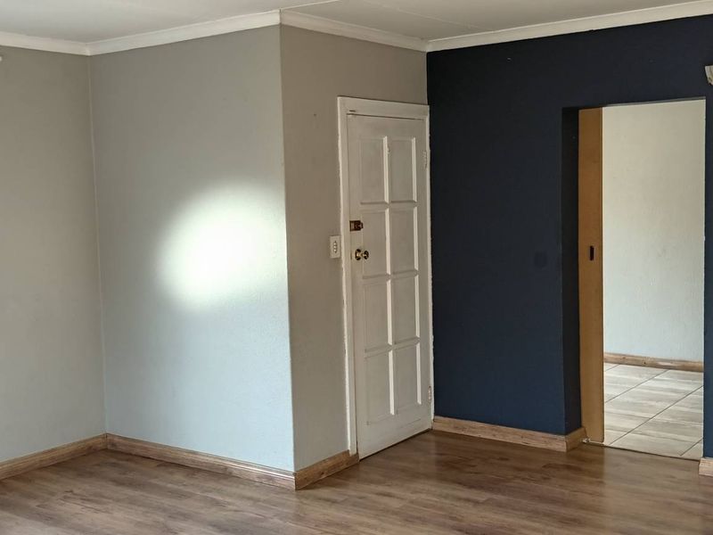 An empty living room featuring laminate flooring, a distinctive circular window, and a transition through to an adjacent tiled space.