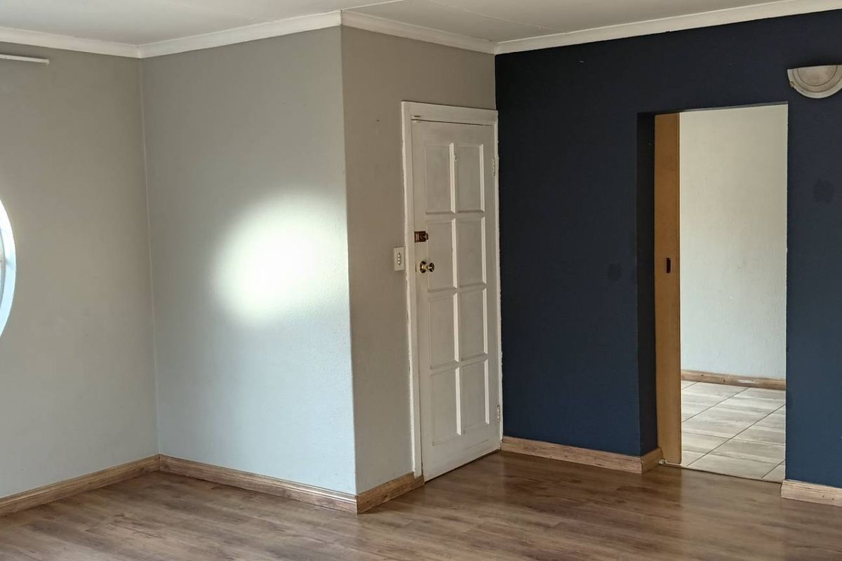 An empty living room featuring laminate flooring, a distinctive circular window, and a transition through to an adjacent tiled space.