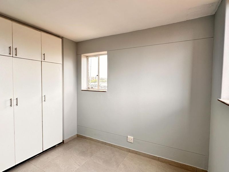 A clean, empty bedroom featuring neutral grey walls, tiled flooring, and ample built-in cupboard storage space.