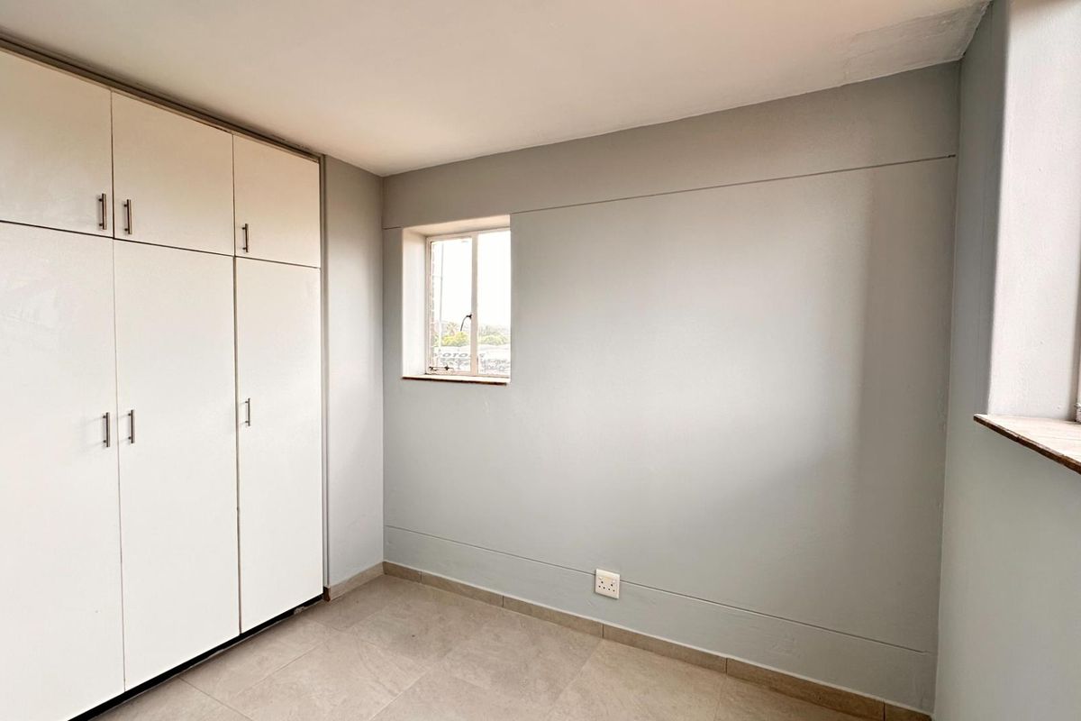 A clean, empty bedroom featuring neutral grey walls, tiled flooring, and ample built-in cupboard storage space.