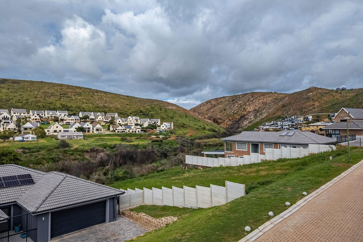 Aerial view of a residential townhouse complex featuring tiled roofs, solar panels, and paved driveways set against a scenic hilly landscape.
