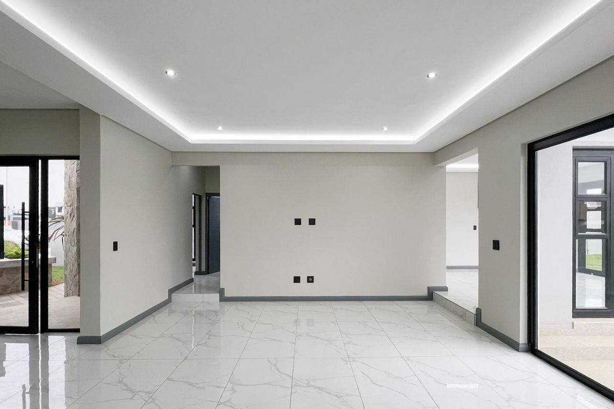 Spacious, modern living area featuring high-gloss marble-look floor tiles, recessed cove lighting, and large black aluminium sliding doors providing seamless outdoor access.