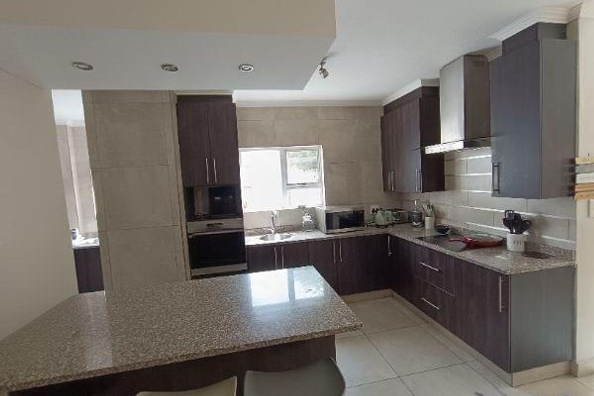 Modern kitchen featuring dark cabinetry, granite countertops, a central island, built-in oven, and stainless steel extractor fan.
