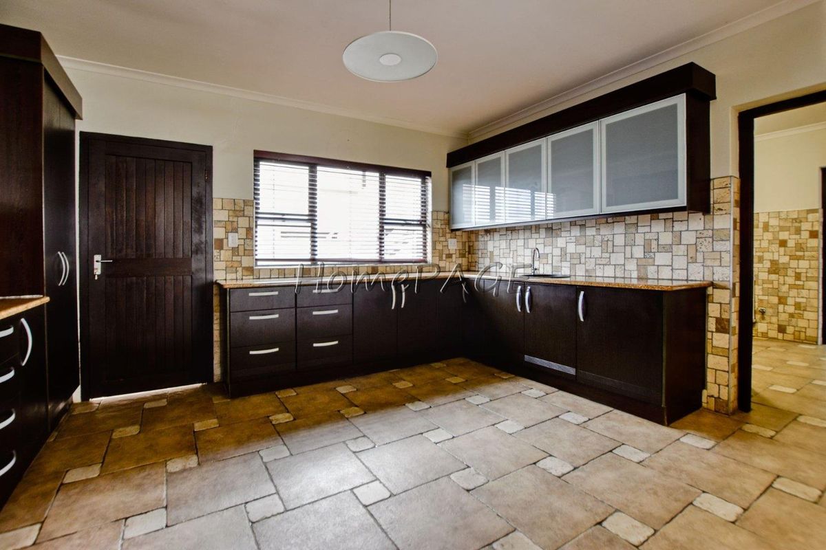 A spacious kitchen featuring dark wood cabinetry, stone tile flooring, a tiled backsplash, and ample counter space with an integrated sink.
