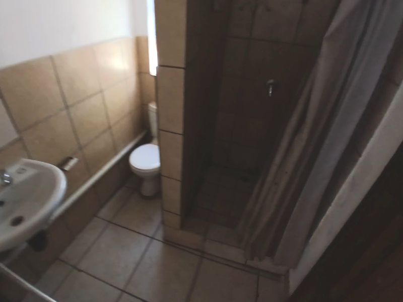 A dated bathroom featuring a pedestal basin, toilet, and a tiled shower enclosure with a curtain.