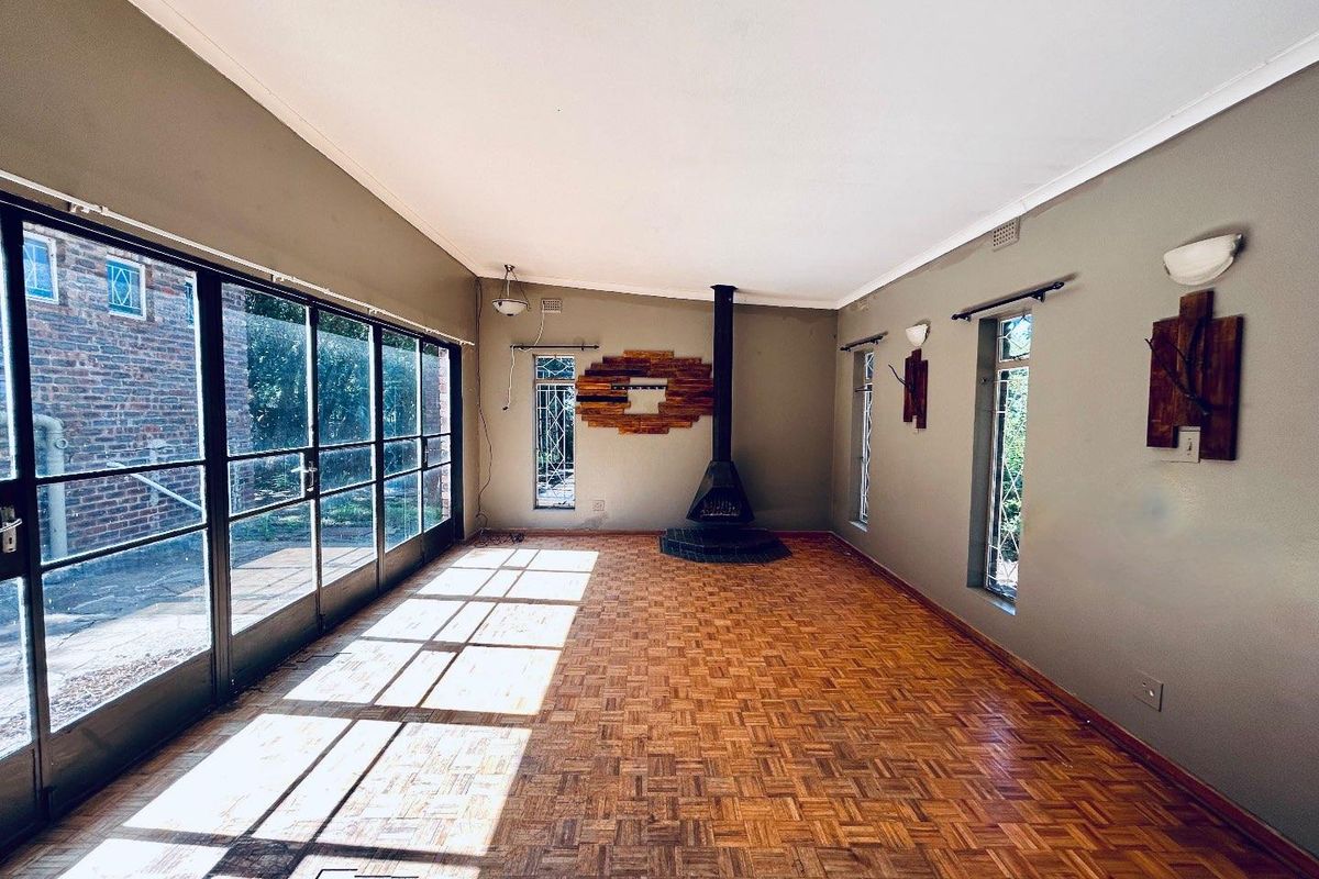Spacious living room featuring original parquet flooring, a freestanding fireplace, and large glass sliding doors providing ample natural light and garden access.