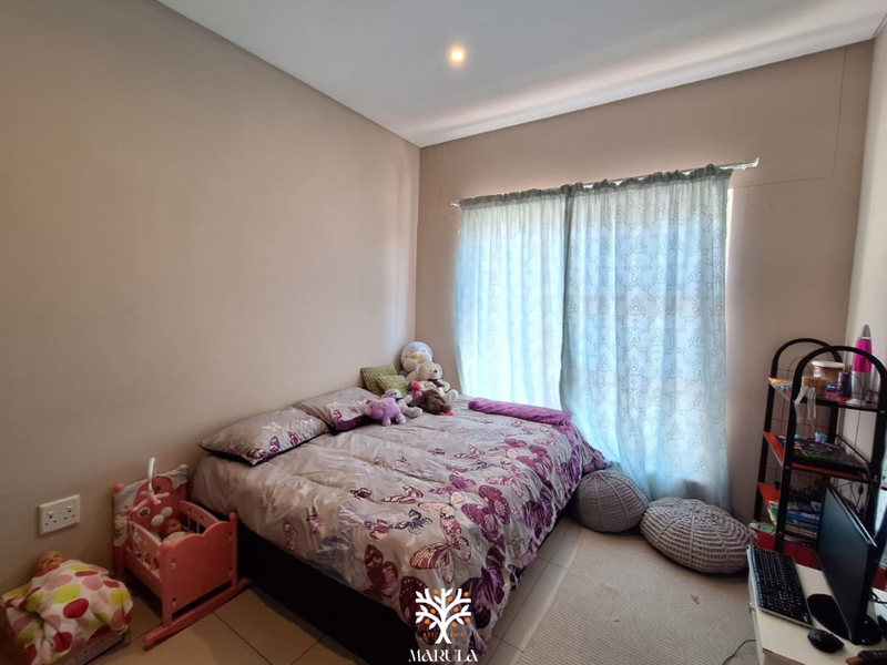 A well-maintained bedroom featuring neutral wall tones, tiled flooring, and large windows with installed curtain tracks, providing a bright and functional living space.