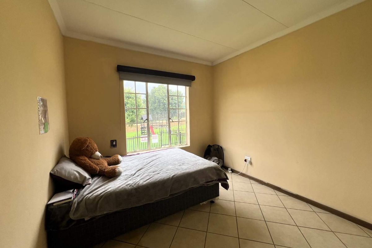 A simple bedroom featuring tiled flooring, a window with a roller blind, and neutral wall paint.