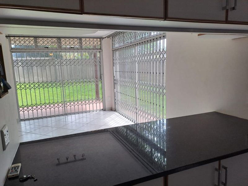 Open plan living area featuring a granite countertop kitchen island, tiled flooring, and secure sliding glass doors leading to the rear garden.