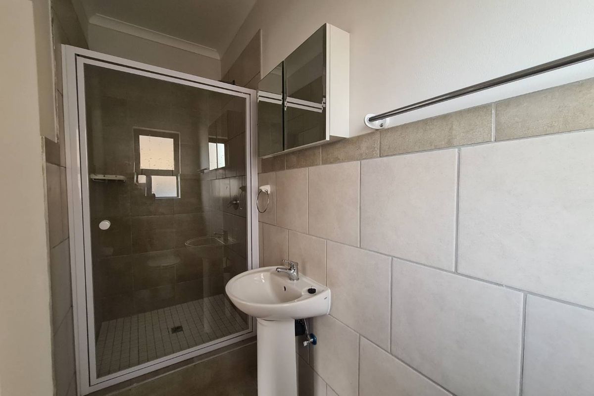 A clean, functional bathroom featuring a pedestal sink, a glass-enclosed shower, and a mirrored medicine cabinet with neutral wall tiling.