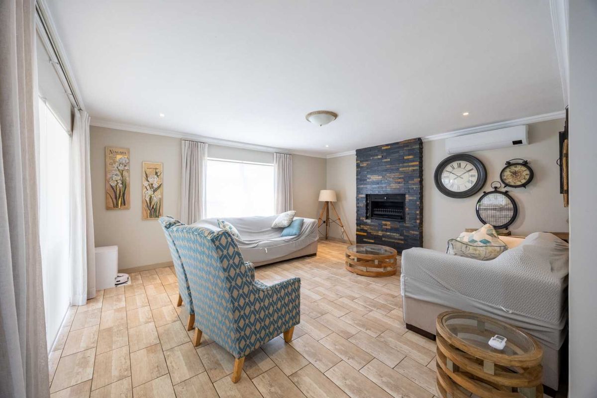 Spacious living room featuring a striking stone-clad fireplace, neutral tiled flooring, and a wall-mounted air conditioning unit with access to an outdoor area.