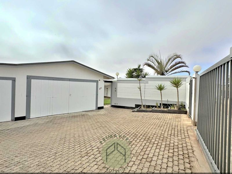 Front exterior view featuring a paved driveway, double garage, and secure boundary wall with metal gate access.