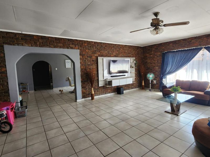 Spacious living room featuring exposed brick walls, tiled flooring, a ceiling fan, and a built-in media console, offering a rustic and functional living space.