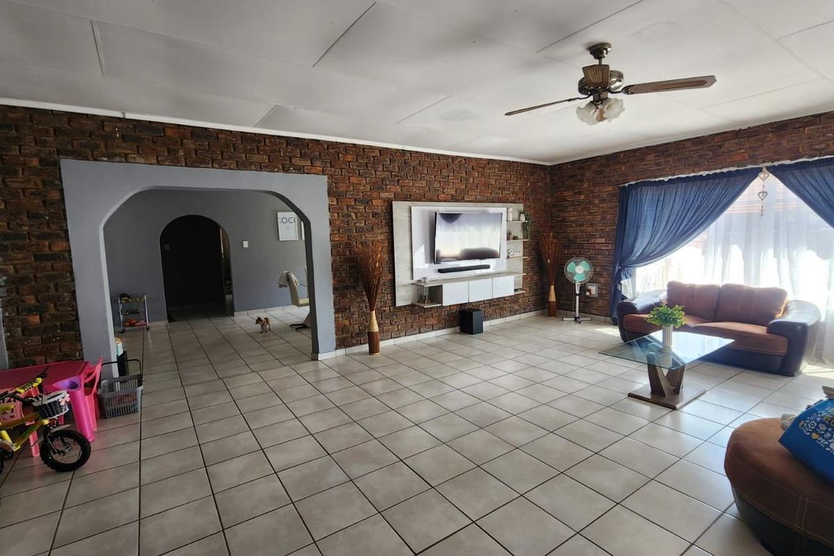 Spacious living room featuring exposed brick walls, tiled flooring, a ceiling fan, and a built-in media console, offering a rustic and functional living space.