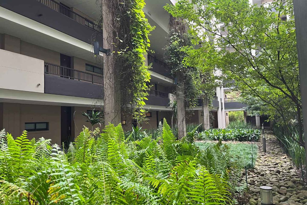 A view of the apartment complex exterior featuring landscaped garden areas, stone pathways, and multi-level balconies with climbing greenery.